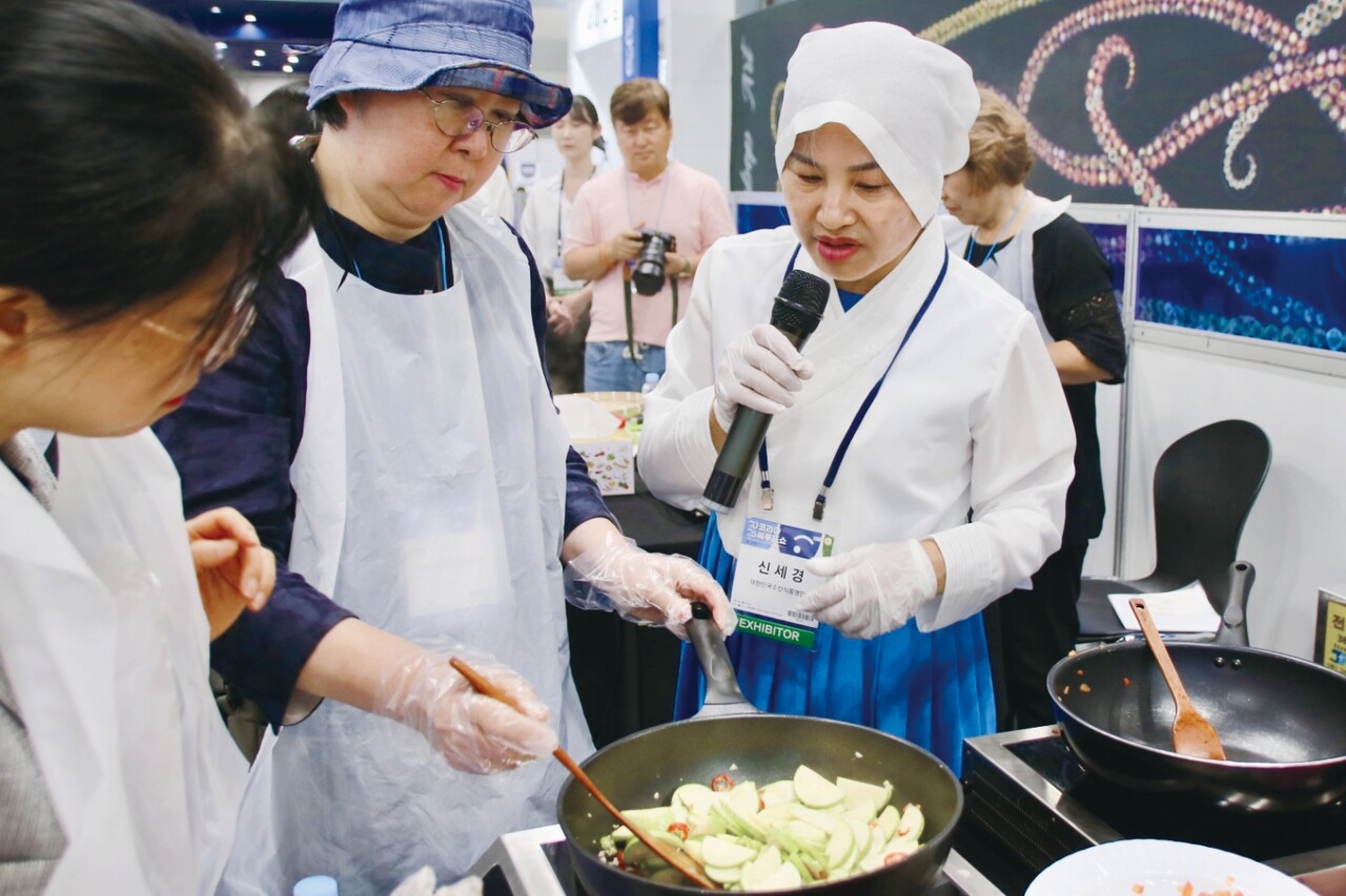 신세경 명인이 새우젓에 관한 이야기를 마치고, 새우젓으로 만들 수 있는 여름철 반찬 중 하나인 호박볶음을 체험객들에게 설명하고 있다.
